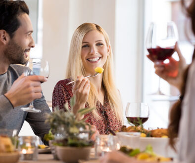 A Young Woman Holding a Potato on Her Fork While Enjoying Dinner With Her Friends Living With IBS