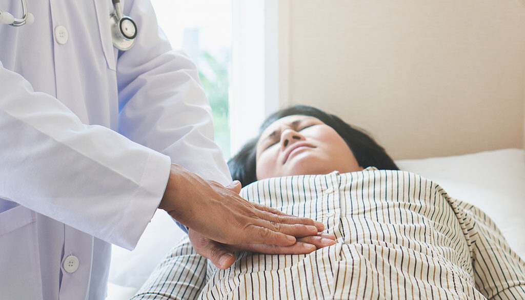 Closeup of a Woman Laying on an Exam Table With a Gastroenterologist Pressing Their Hands Into Her Stomach Women’s Gastrointestinal Health