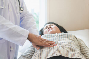 Closeup of a Woman Laying on an Exam Table With a Gastroenterologist Pressing Their Hands Into Her Stomach Women’s Gastrointestinal Health