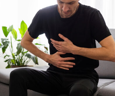 A Man Sitting On A Couch Holding His Upper Abdominal Area Can Gallstones Cause Acid Reflux